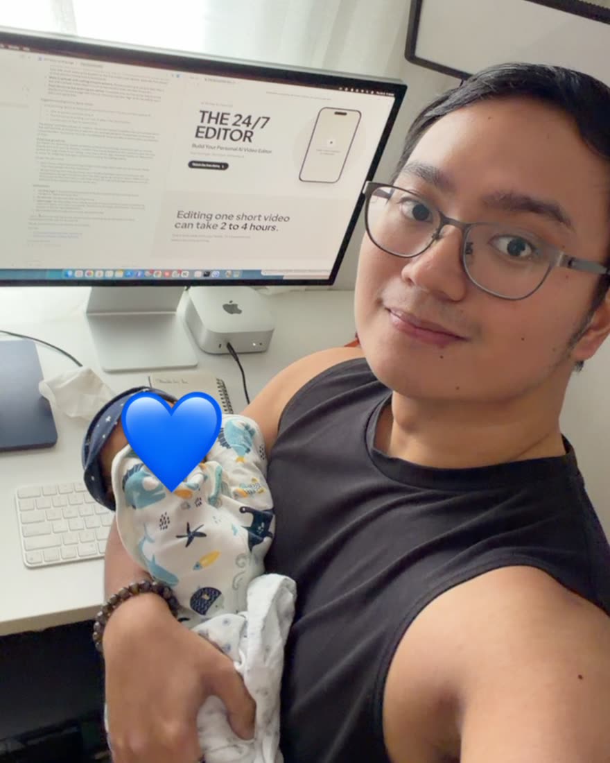 Alec Cuenca at his desk at home, holding his baby son, with THE 24/7 EDITOR page on the screen behind him